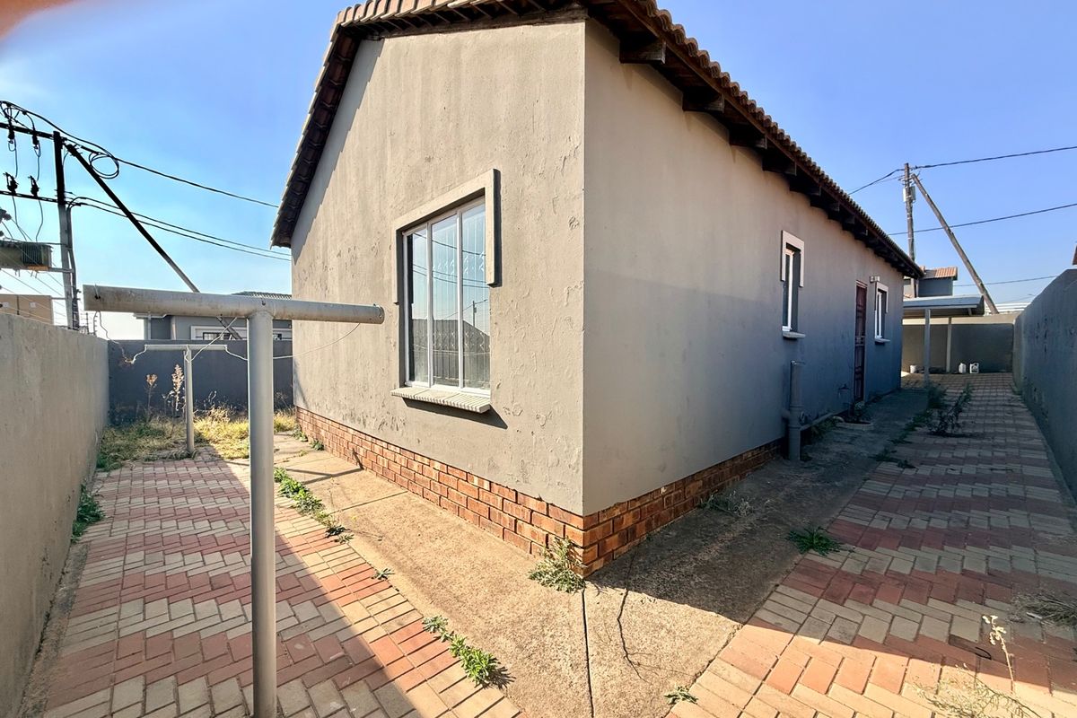 Rear exterior view of the house featuring a paved walkway, brick plinth, and a metal washing line against a boundary wall.