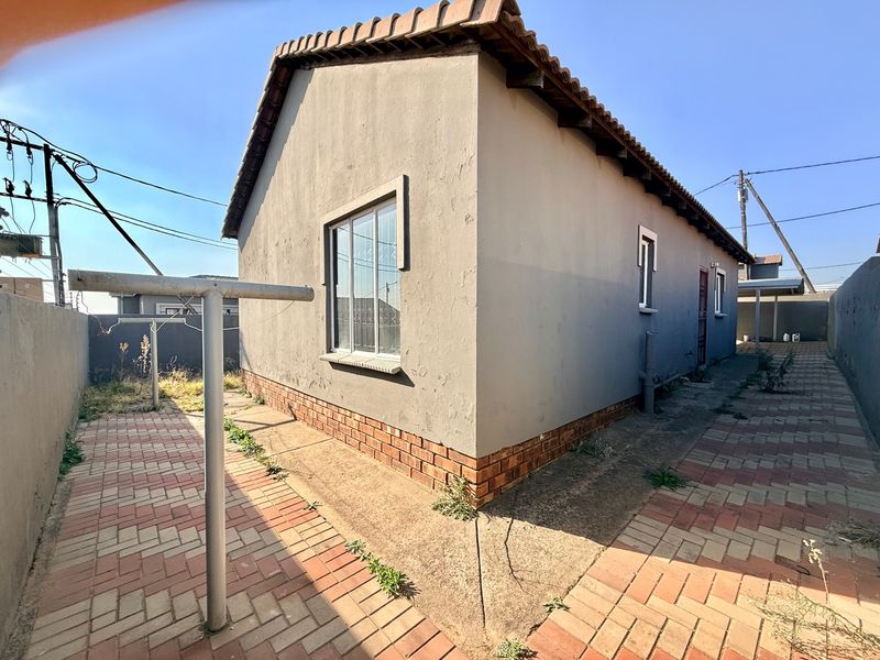 Rear exterior view of the house featuring a paved walkway, brick plinth, and a metal washing line against a boundary wall.