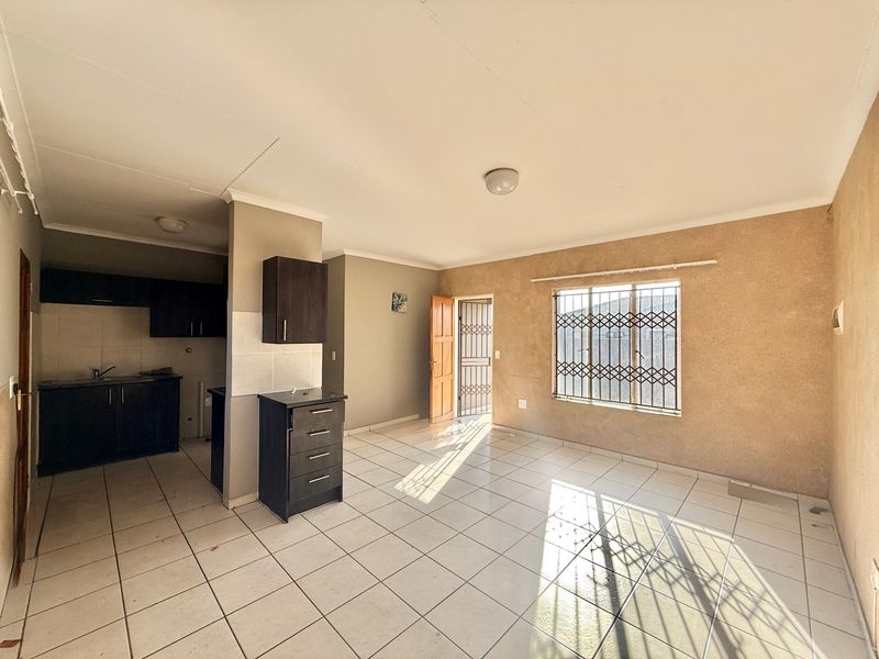 Open-plan living area featuring tiled flooring, built-in kitchen cabinetry, and security features on windows and doors, presenting a blank canvas for renovation.