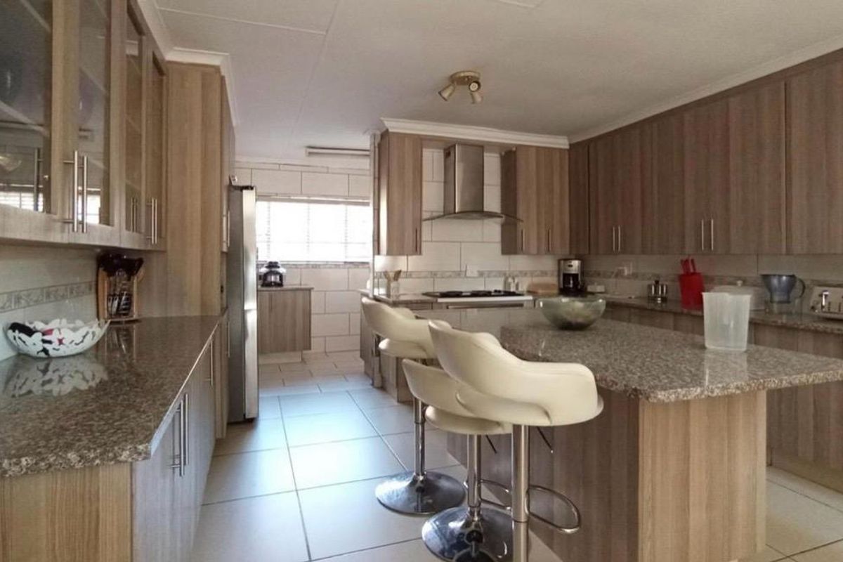 A spacious kitchen featuring wood-finish cabinetry, granite countertops, a central island with breakfast bar seating, and tiled flooring throughout.