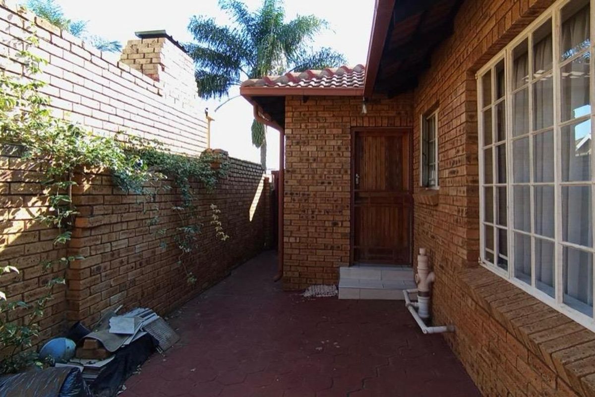 A rear exterior view of the house featuring face brick walls, a paved patio area, and a secure wooden entrance door.
