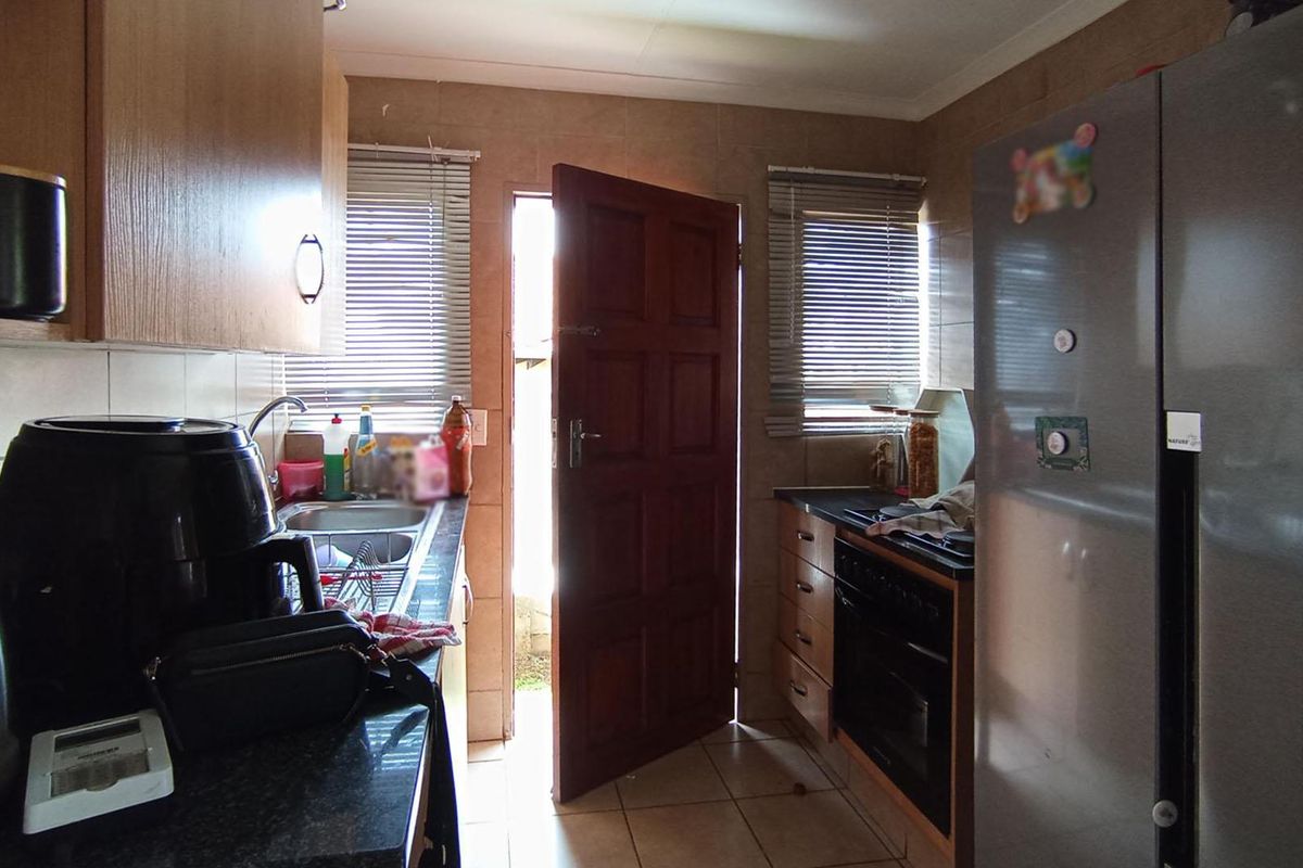 A functional kitchen featuring built-in cabinetry, laminate countertops, a stainless steel sink, and a built-in oven with tiled flooring and backsplash.