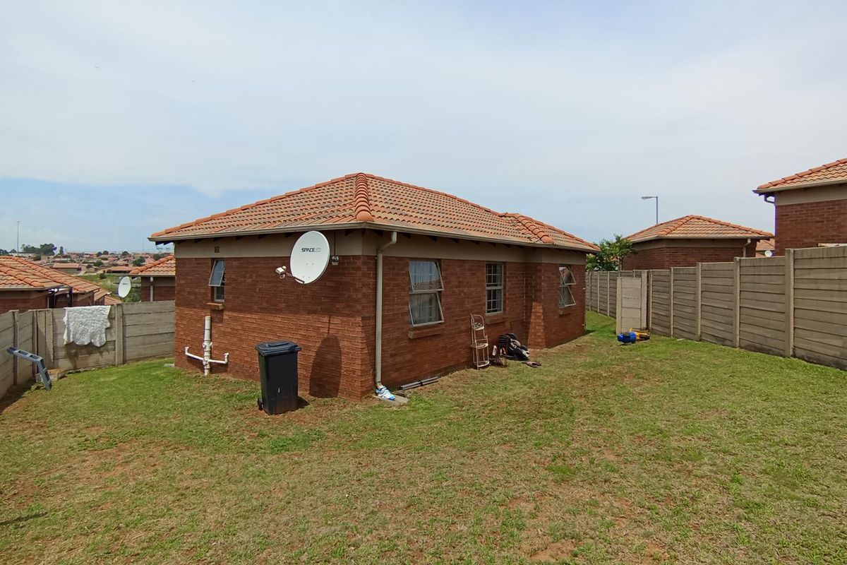 Rear view of a facebrick house featuring a terracotta tiled roof, casement windows, and a private garden enclosed by precast concrete boundary walls.