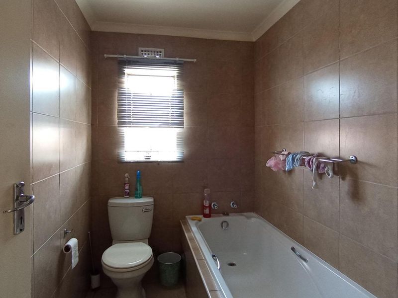 A functional bathroom featuring full-height ceramic wall tiling, a built-in bathtub, and a standard toilet suite.