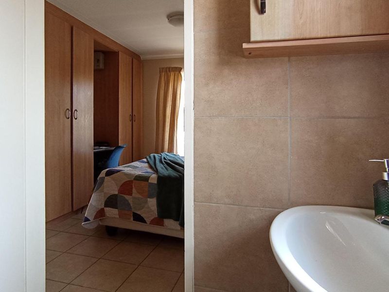 A bedroom featuring built-in cupboards and tiled flooring, with an adjacent bathroom area visible through the doorway.