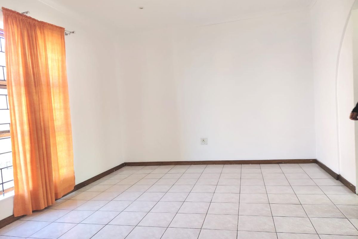 A bright, empty living room featuring neutral tiled flooring, recessed downlighting, and clean white walls, offering a versatile blank canvas for interior design.