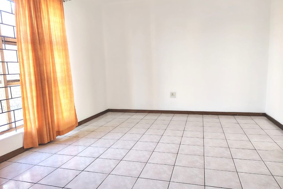 A bright, empty bedroom featuring neutral tiled flooring and a window with security bars, providing a clean canvas for personalization.