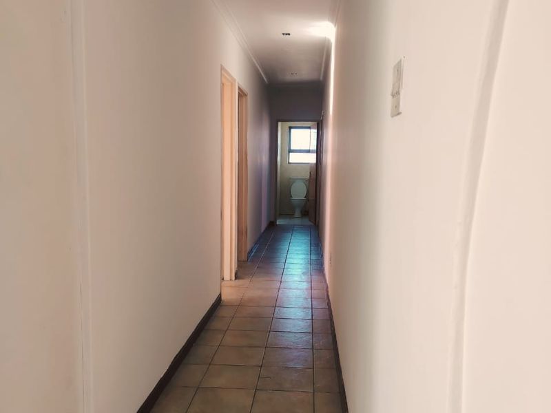 A long, empty hallway featuring tiled flooring and recessed downlights, providing access to adjacent rooms.