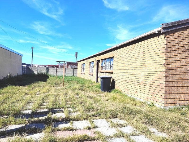 Rear exterior view of a face brick house featuring a large backyard with concrete paving and a precast boundary wall.