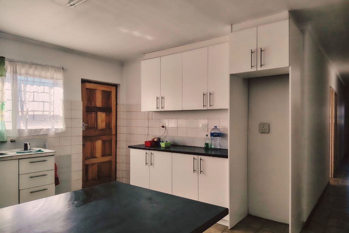 A functional kitchen featuring white built-in cabinetry, dark countertops, tiled backsplash, and tiled flooring with direct access to an exterior door.