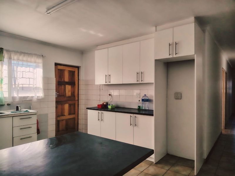 A functional kitchen featuring white built-in cabinetry, dark countertops, tiled backsplash, and tiled flooring with direct access to an exterior door.