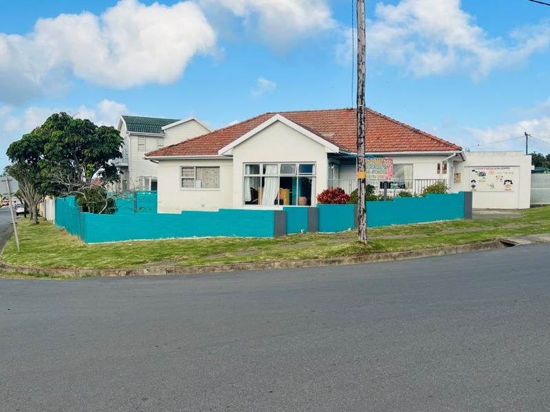A corner-lot residential property featuring a tiled roof, white exterior walls, and a prominent teal boundary wall.