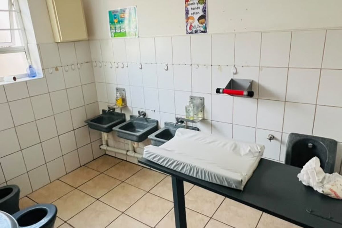A functional bathroom facility featuring multiple small-scale sinks and toilets, suitable for a childcare or educational environment, with tiled surfaces throughout.