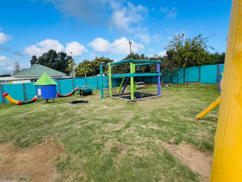 Spacious outdoor garden area featuring a lawn and established playground equipment, enclosed by a precast concrete boundary wall.