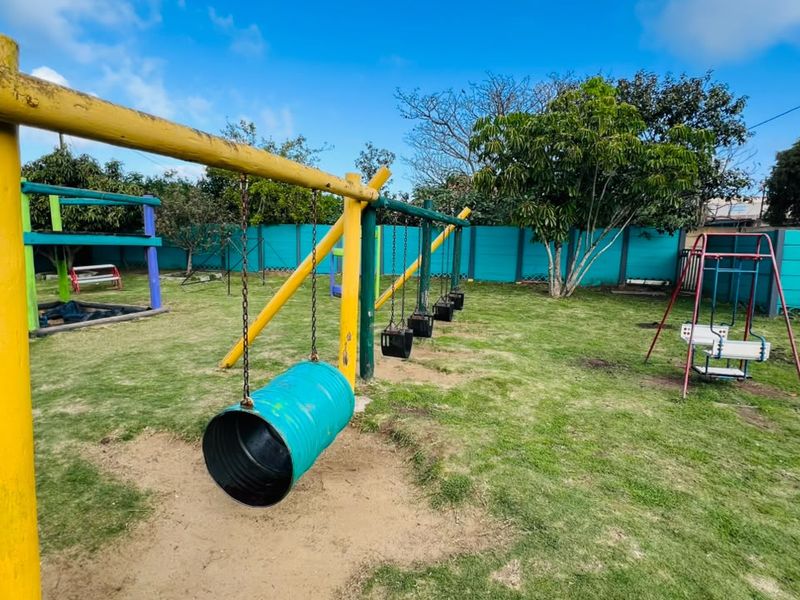 A spacious outdoor garden area featuring a variety of fixed playground equipment and a perimeter boundary wall.
