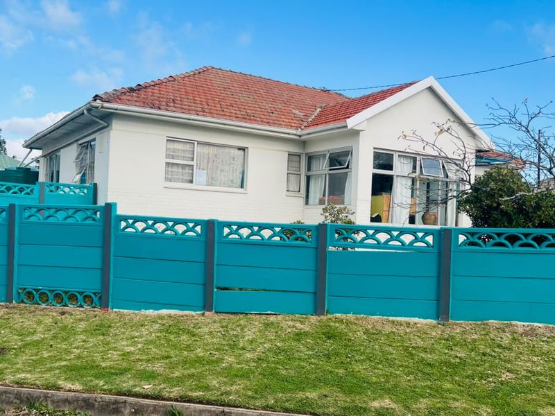 Front elevation of a single-story house featuring a tiled roof, white painted exterior walls, and a prominent teal precast concrete boundary wall.