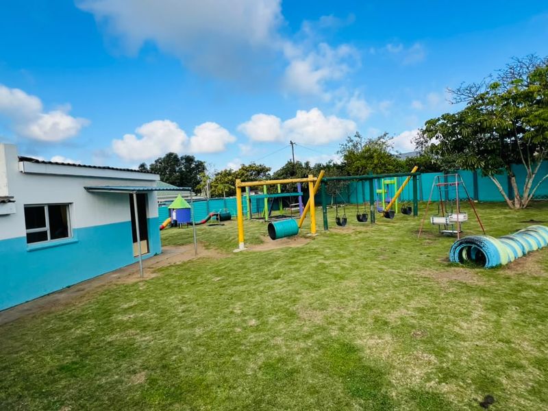 Spacious outdoor garden area featuring a lawn and established playground equipment, enclosed by a perimeter wall.