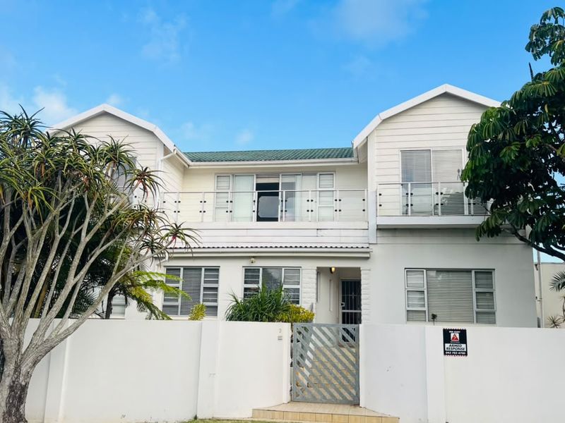 A two-story residential property featuring a white facade, upper-level balconies with metal railings, and a secure perimeter wall with a gated entrance.