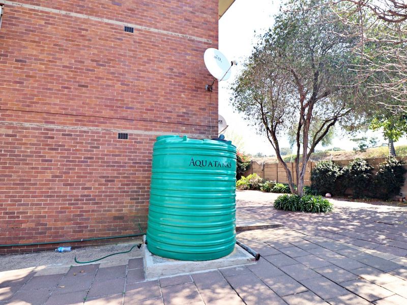 Rear exterior view of the apartment building featuring a brick facade, paved patio area, and a green water storage tank.