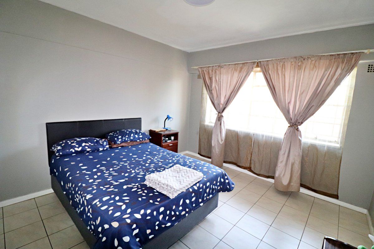 A functional bedroom featuring neutral wall tones, tiled flooring, and a large window allowing for natural light.