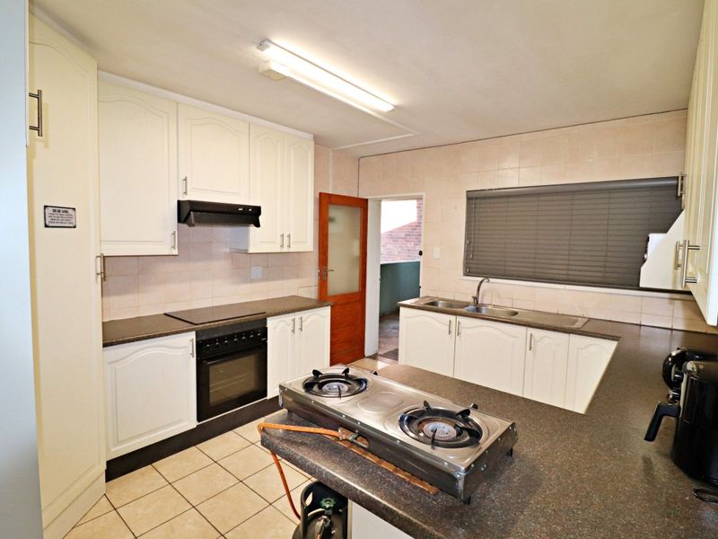 Functional kitchen featuring white cabinetry, dark laminate countertops, built-in oven with extractor, and tiled flooring, offering a practical layout for daily meal preparation.