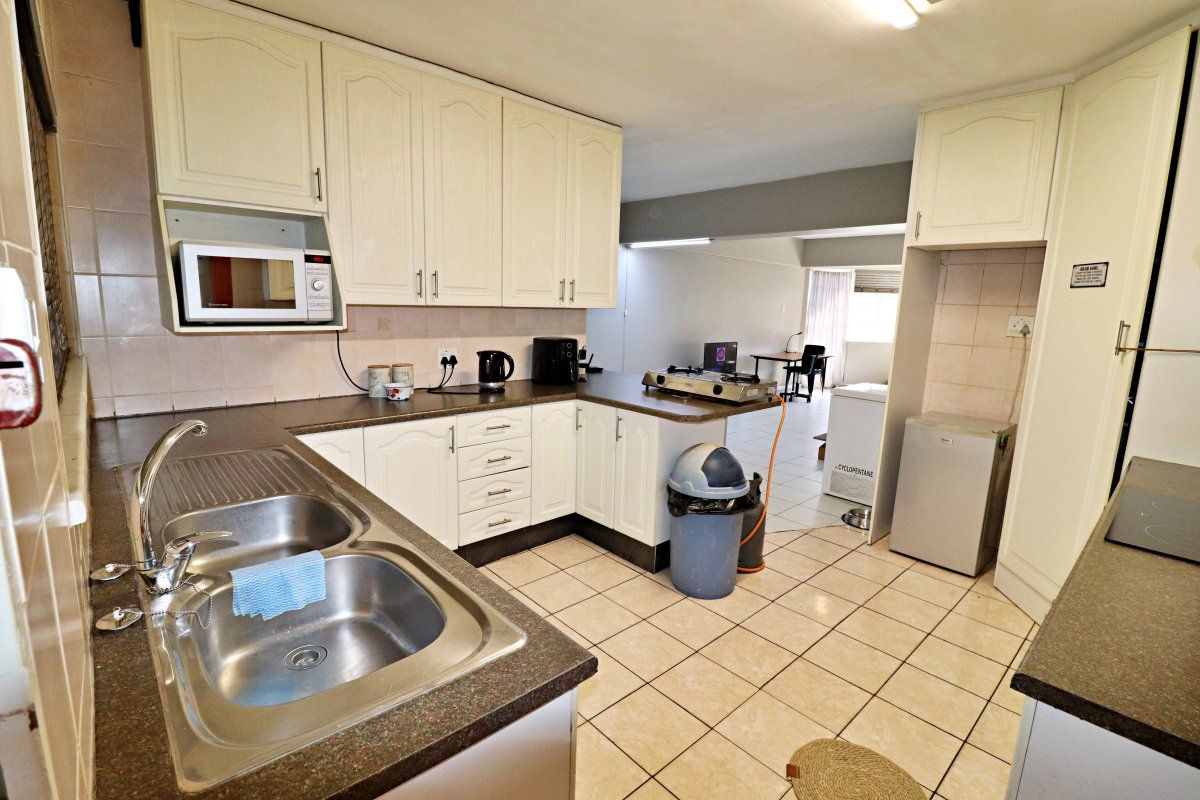 A functional kitchen featuring double bowl stainless steel sink, laminate countertops, built-in cabinetry, and tiled flooring, offering a practical layout for daily use.