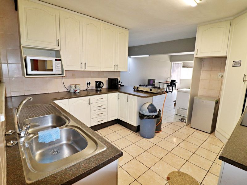 A functional kitchen featuring double bowl stainless steel sink, laminate countertops, built-in cabinetry, and tiled flooring, offering a practical layout for daily use.