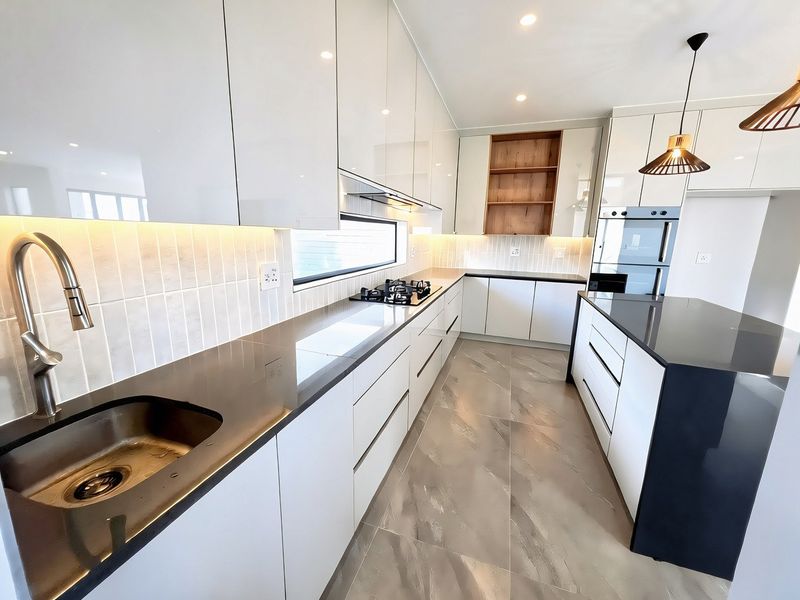Modern kitchen featuring high-gloss cabinetry, stone countertops, a gas hob, built-in oven, and a central island with integrated sink and premium finishes.