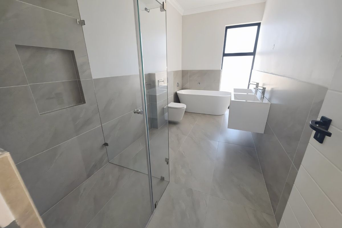 Modern, spacious bathroom featuring a freestanding bathtub, wall-mounted double vanity, walk-in shower with glass screen, and contemporary grey tiling throughout.