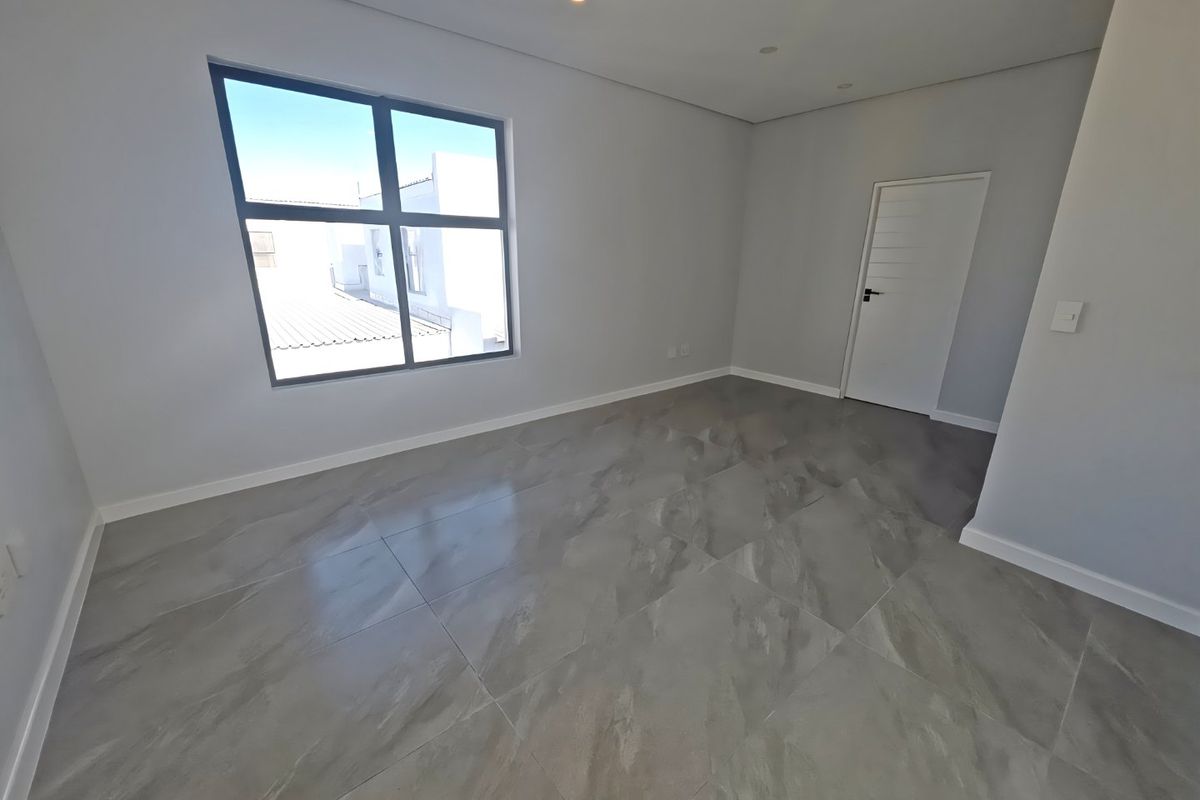A bright, modern, and empty bedroom featuring large format grey floor tiles, neutral walls, and recessed downlighting.