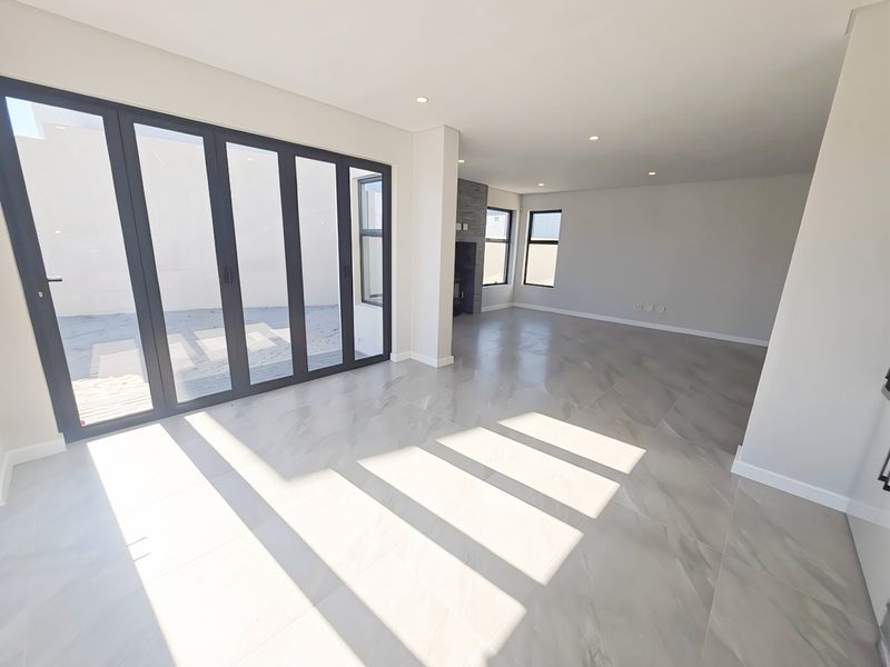 Spacious, light-filled living area featuring large format floor tiles, modern recessed lighting, a stone-clad fireplace, and expansive aluminium stacker doors leading to the exterior.