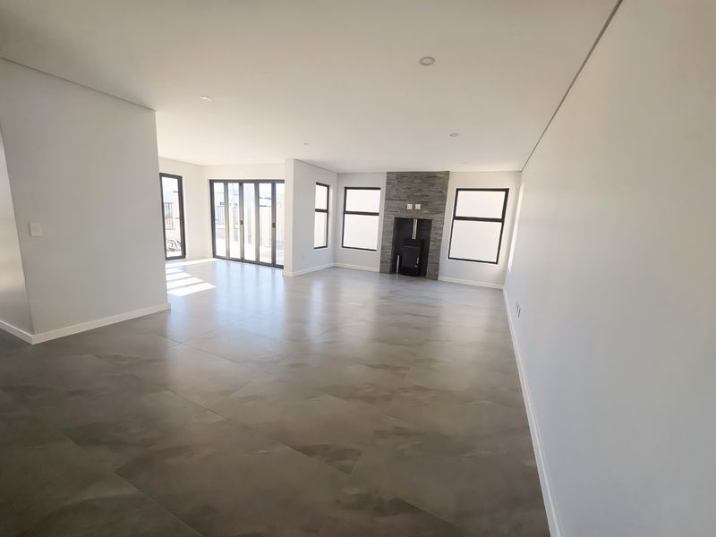 Spacious, modern open-plan living area featuring large format floor tiles, a stone-clad fireplace with a built-in stove, and expansive aluminium sliding doors.