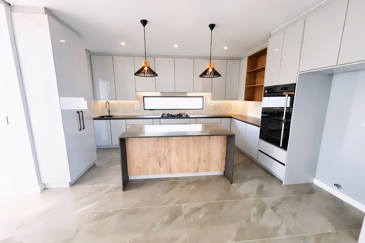 Modern kitchen featuring sleek white cabinetry, a central island with wood-look finish, integrated oven, gas cooktop, and large format tiled flooring.