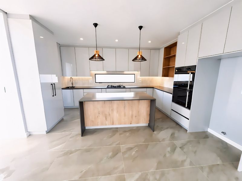 Modern kitchen featuring sleek white cabinetry, a central island with wood-look finish, integrated oven, gas cooktop, and large format tiled flooring.