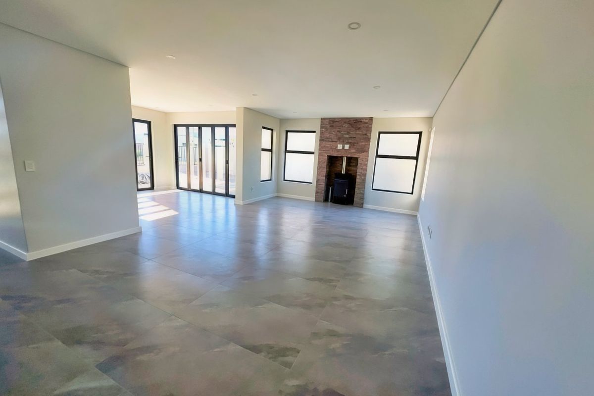 Spacious, modern living area featuring large format floor tiles, a stone-clad fireplace with a wood-burning stove, and expansive aluminium stacker doors leading outdoors.