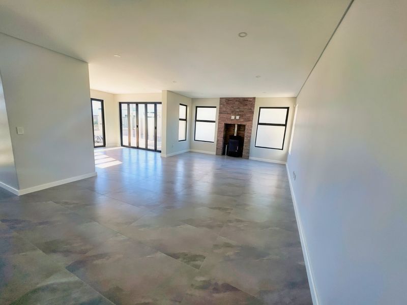 Spacious, modern living area featuring large format floor tiles, a stone-clad fireplace with a wood-burning stove, and expansive aluminium stacker doors leading outdoors.
