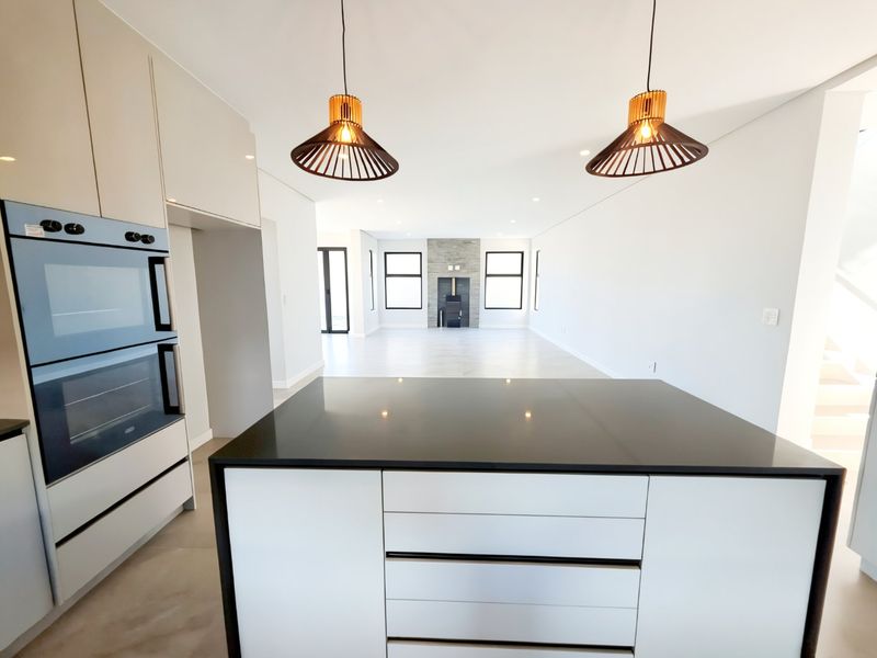 Modern open-plan kitchen and living area featuring a central island, built-in double oven, and a stone-clad fireplace in the spacious lounge.