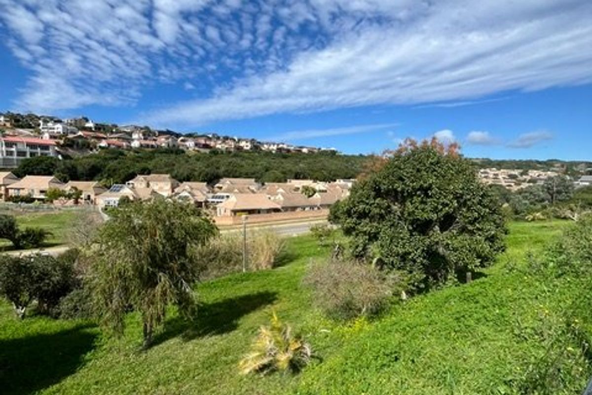 A scenic elevated view overlooking a green landscape and surrounding residential neighborhood under a bright blue sky.