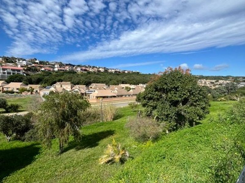 A scenic elevated view overlooking a green landscape and surrounding residential neighborhood under a bright blue sky.
