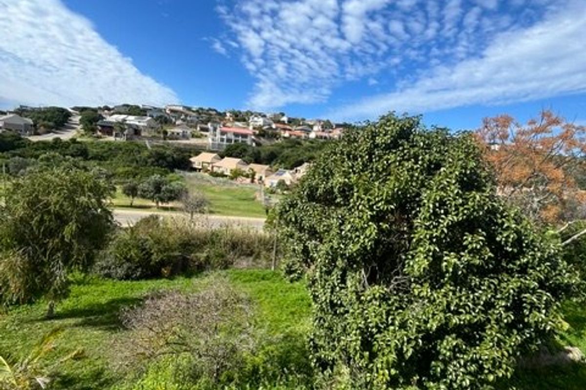 A scenic view overlooking a green garden area with mature trees and a distant residential hillside landscape.
