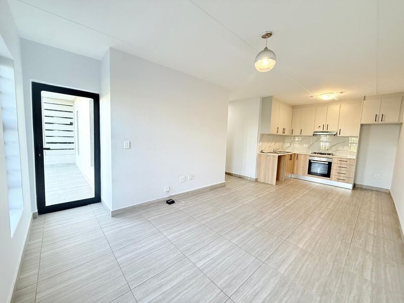 Modern open-plan living area featuring a sleek kitchen with built-in appliances, neutral tiled flooring, and direct access to an outdoor patio space.