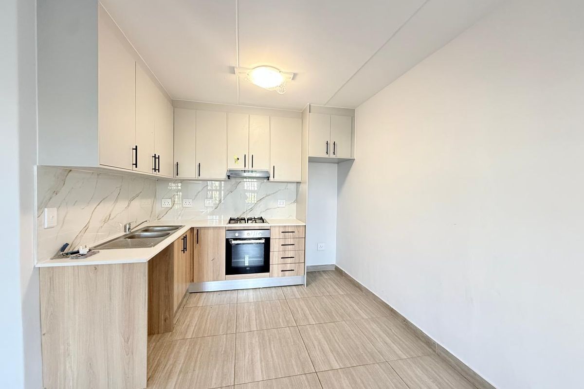 Modern kitchen featuring light wood-tone cabinetry, marble-look splashback, built-in oven, gas hob, and neutral tiled flooring in an open-plan layout.