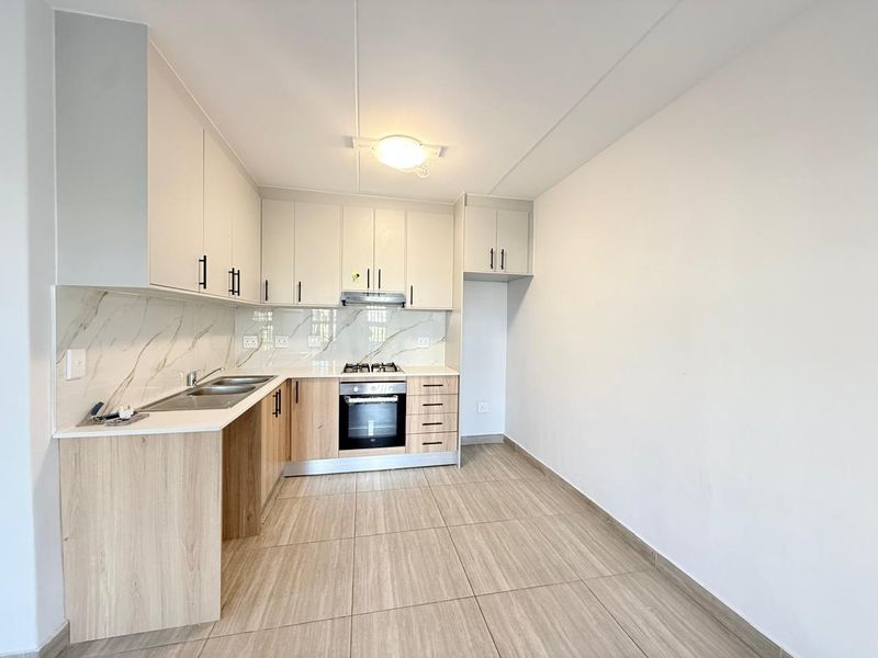 Modern kitchen featuring light wood-tone cabinetry, marble-look splashback, built-in oven, gas hob, and neutral tiled flooring in an open-plan layout.