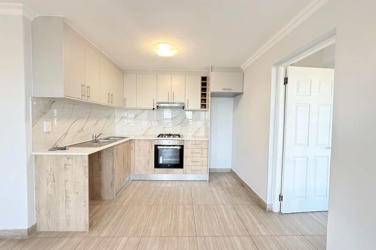 Modern kitchen featuring light wood-tone cabinetry, marble-effect splashback, integrated oven and hob, and neutral tiled flooring in a clean, well-maintained space.