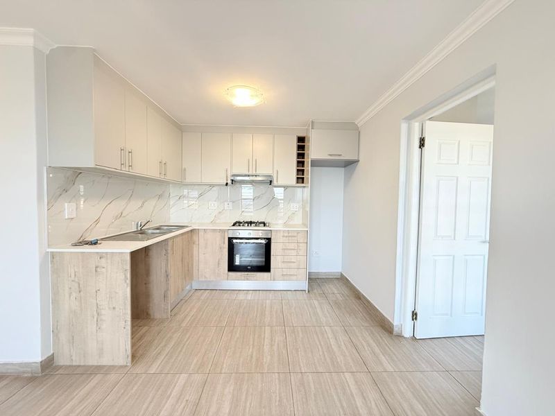 Modern kitchen featuring light wood-tone cabinetry, marble-effect splashback, integrated oven and hob, and neutral tiled flooring in a clean, well-maintained space.