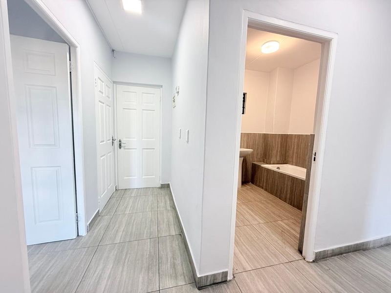 A clean, neutral hallway featuring tiled flooring and multiple panel doors, providing access to adjacent rooms including a bathroom.