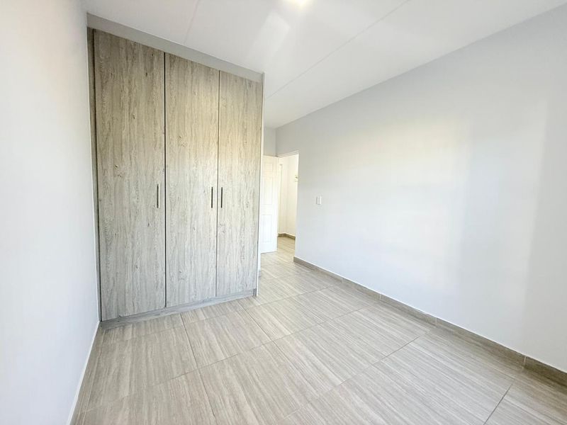 A bright, empty bedroom featuring modern wood-look tiled flooring and built-in cupboards with a neutral finish.
