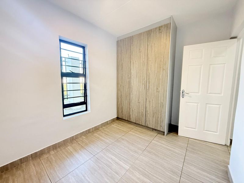 A clean, empty bedroom featuring modern wood-look tiled flooring and built-in cupboards with a neutral finish.