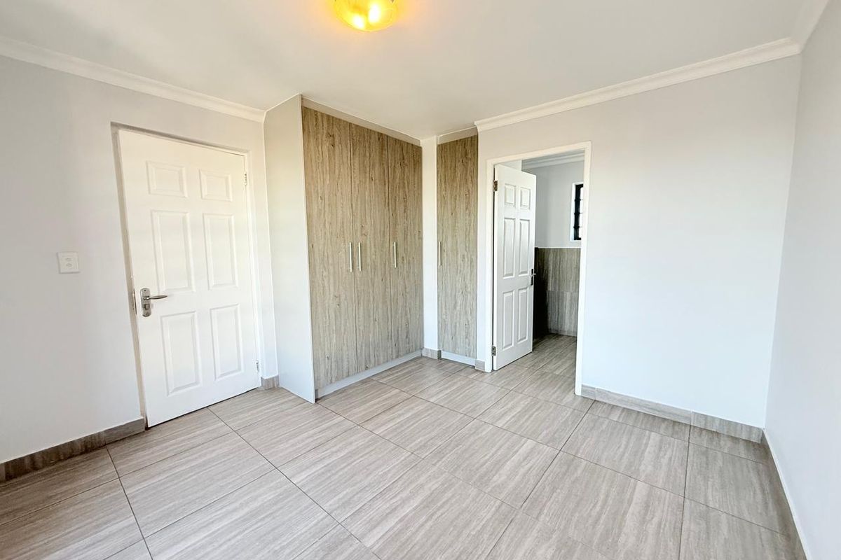 A bright, empty bedroom featuring modern wood-look tiled flooring, built-in cupboards with wood-grain finish, and crisp white walls.
