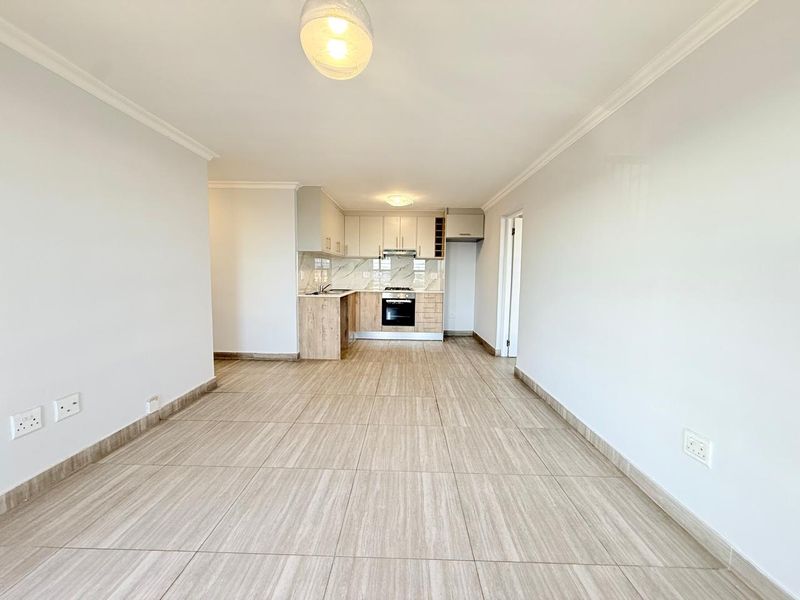 An open-plan living and kitchen area featuring modern cabinetry, built-in oven and hob, and neutral tiled flooring throughout.